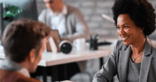 A woman is siting on a desk smiling at a man